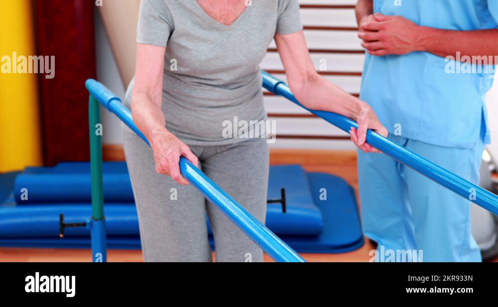Physical therapist watching patient walk with parallel bars Stock Video