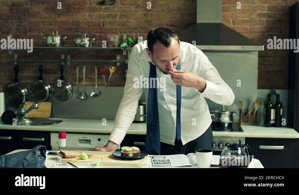 Businessman eating sandwich and reading newspaper in the kitchen HD