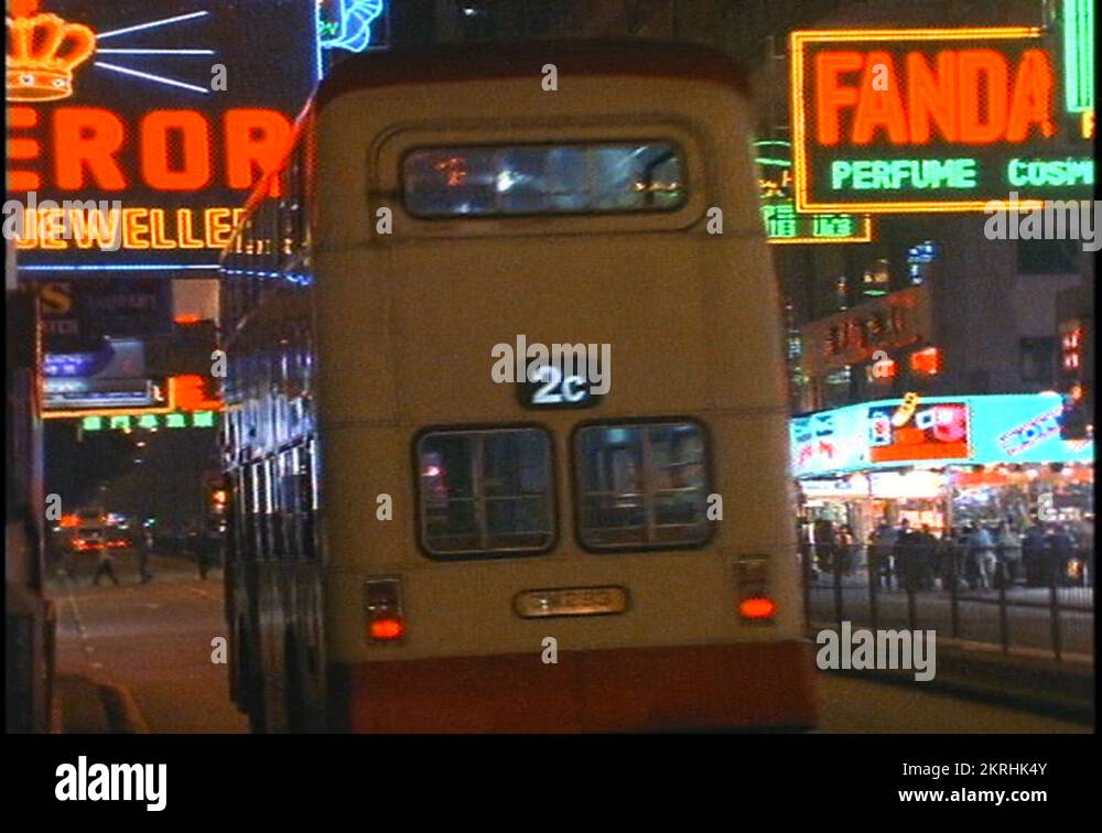 Doubledecker buses drive on a busy street in Hong Kong at night Stock