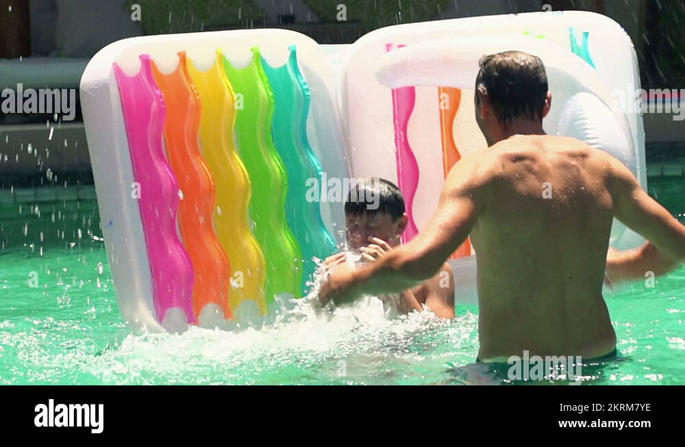 Father throwing his son from air mattress into swimming pool, slow ...