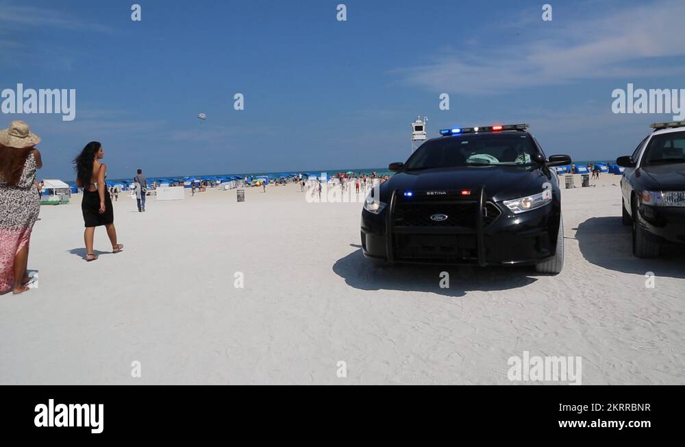 Police Car with Flashing Lights and Beachgoers on Miami Beach Stock