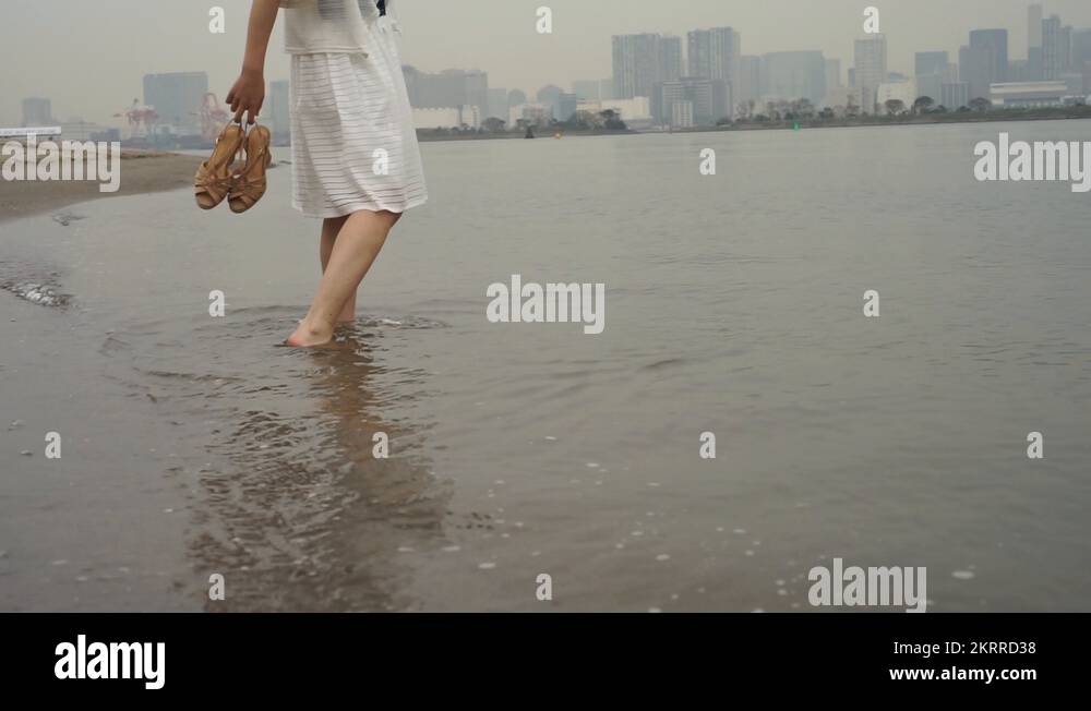 Young Japanese woman barefoot in the water at city beach, Tokyo, Japan ...