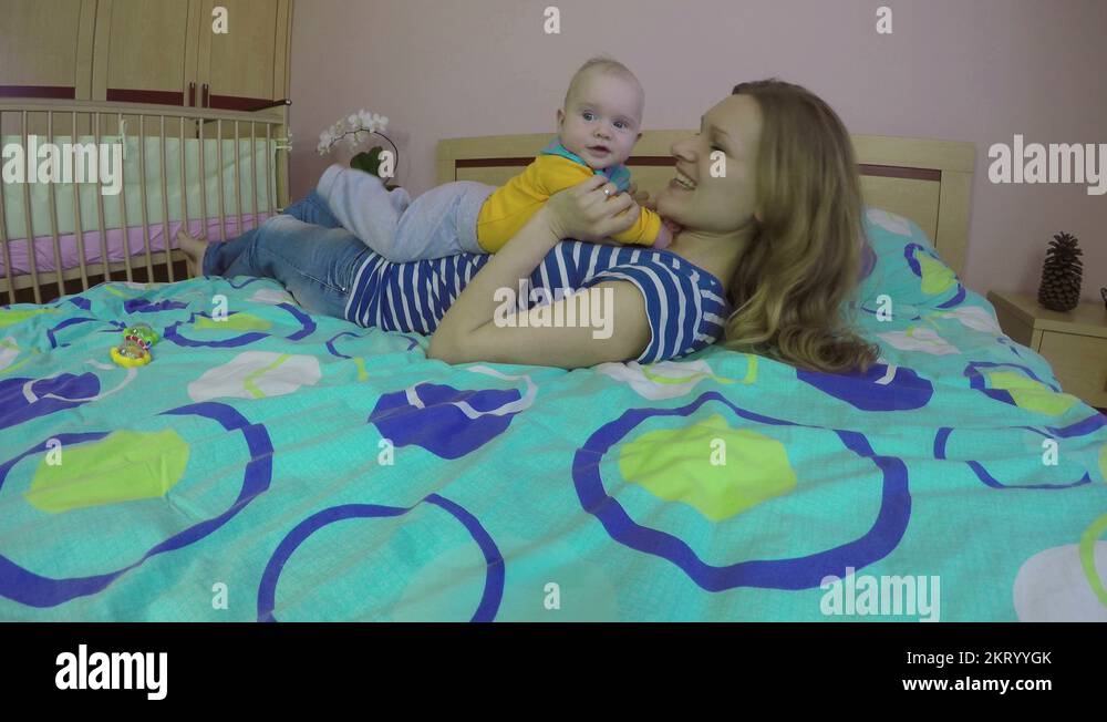 Loving woman and 5 month old baby girl laugh and play on bed. 4K Stock