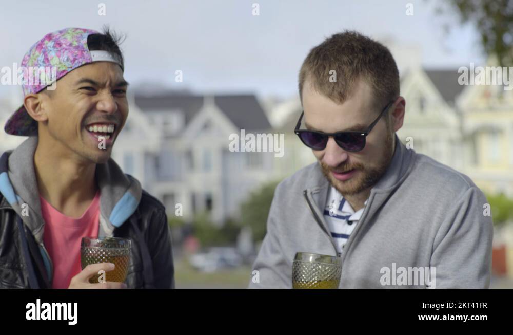 Happy Gay Couple Laugh And Toast With Wine Glasses In Park, They Kiss