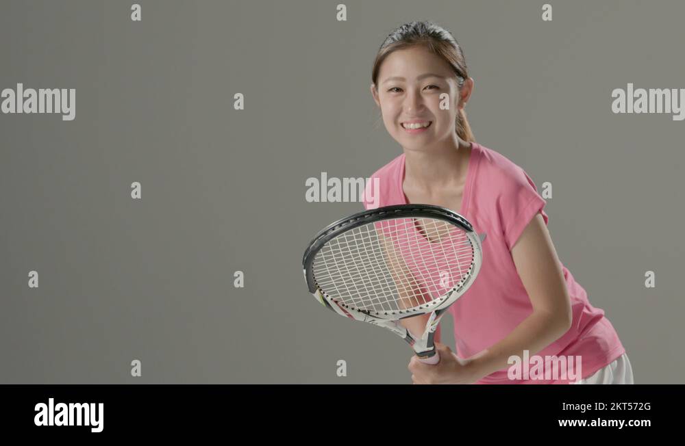 Young Japanese female tennis player in action against grey background