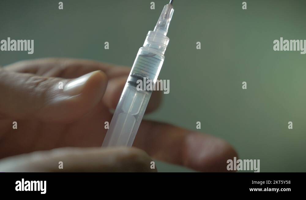 Hand using hypodermic syringe and spraying out liquid in slow motion