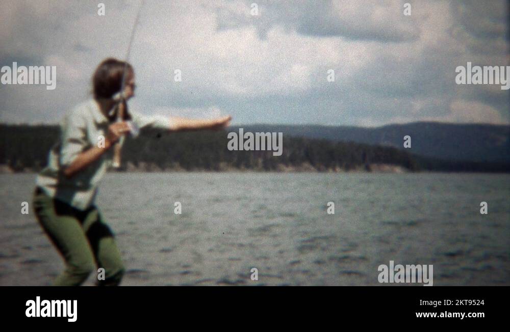 1971 Teenage girl catches trout fish in mountain lake setting Stock