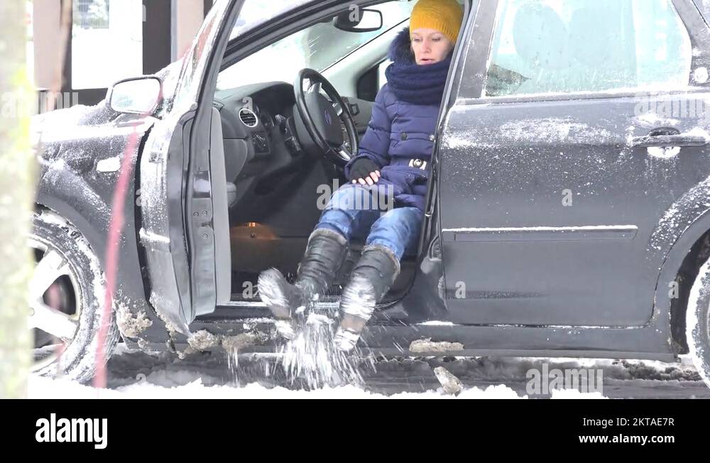 Woman shake off snow from snowy legs before sit in car and close door