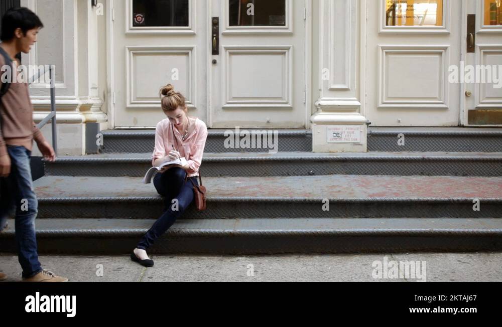 Young woman sitting on steps, man walking past Stock Video Footage Alamy