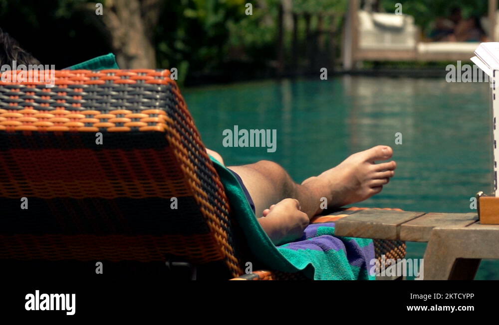 Man relaxing and sunbathing on sunbed by swimming pool Stock Video