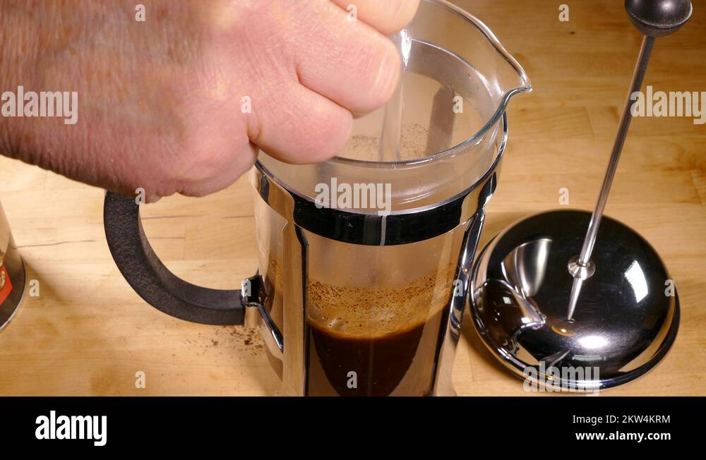 Hand pouring boiling water into a French press, then stirring Stock