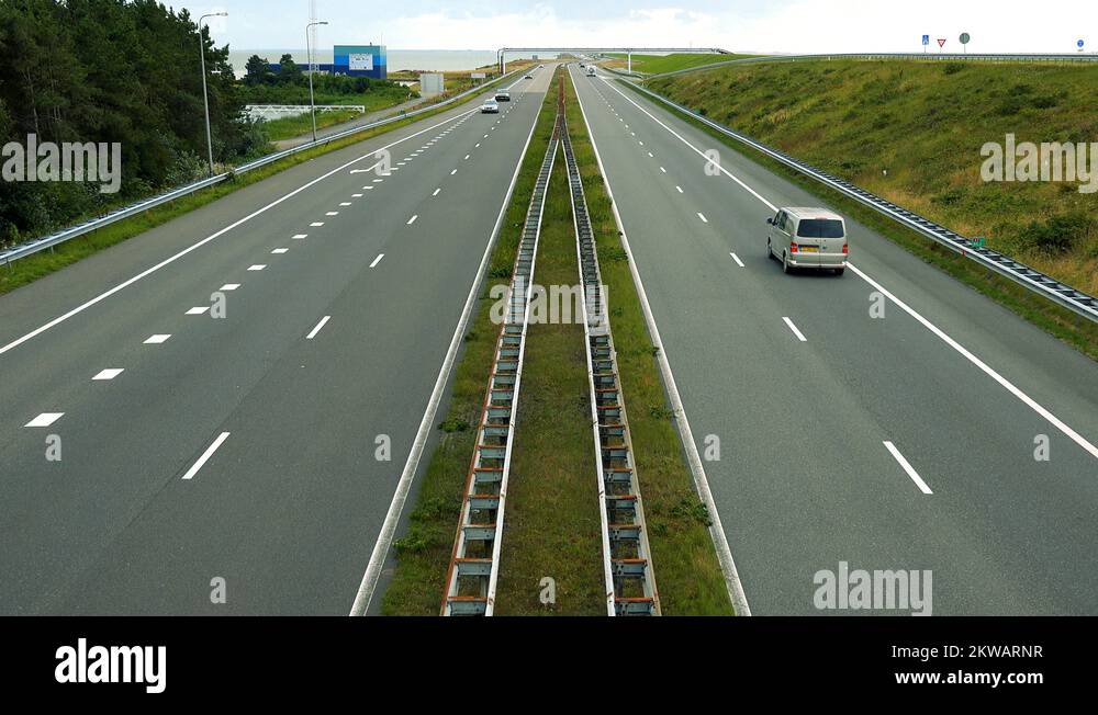 Cars drive down a highway with a forest and a square building on the ...