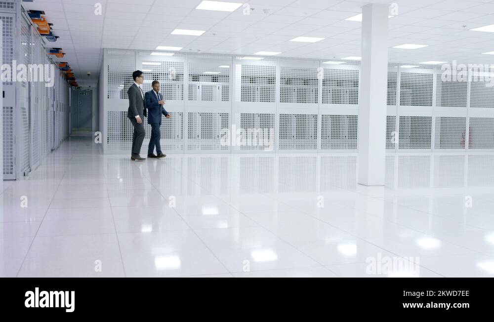 4K Business people looking around large data center with rows of server ...