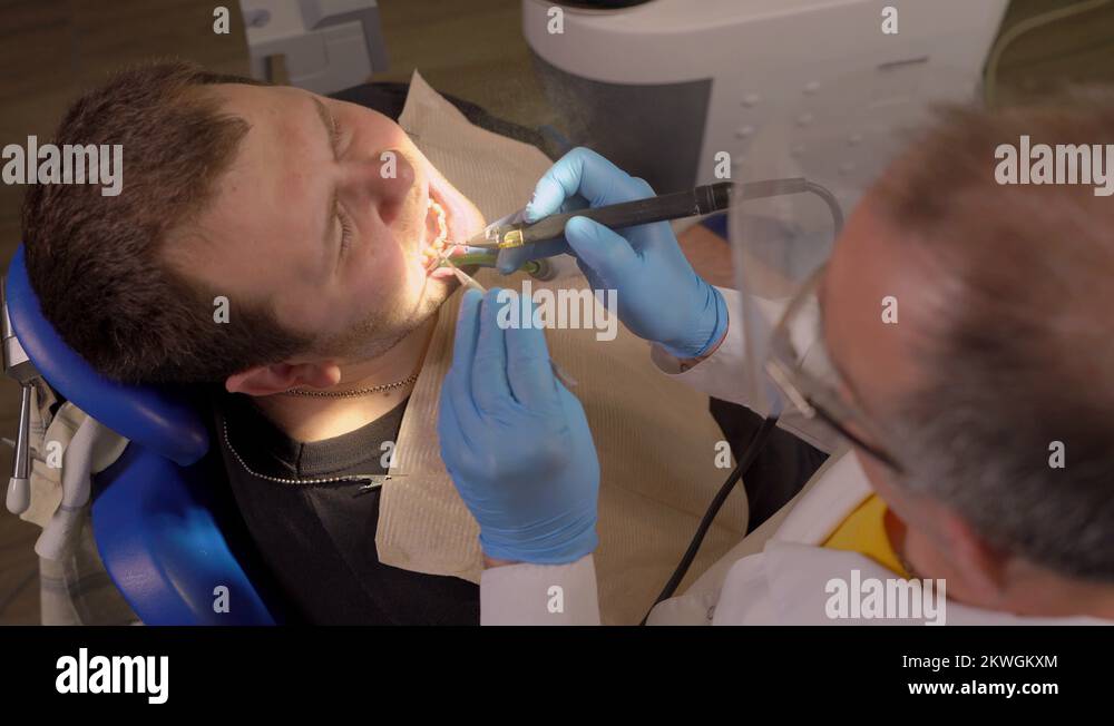 Dentist in Glasses Using Dental Sandblasting Cleans the Patient's Teeth