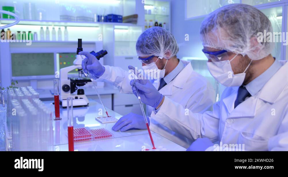 Team of Researchers Men Use Micropipette Pouring Liquid in Microplate