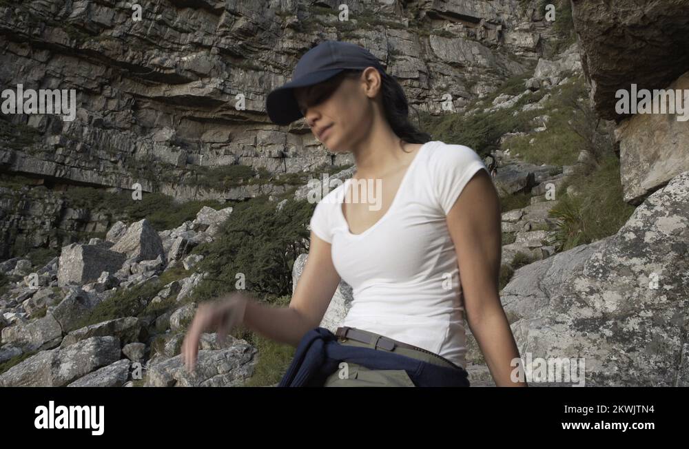 4K Fit & active woman climbing rocky hill top stopping to take a rest