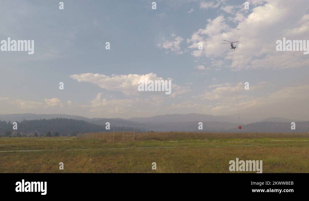 Firefighting helicopter with water bucket taking off from small pond in