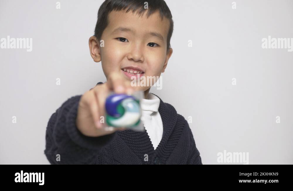 Smiling Asian child giving a washing powder pod to the camera