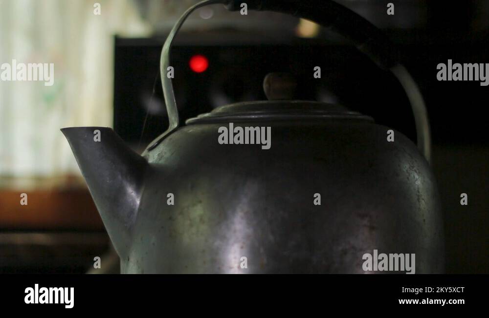 Lifting the lid off of a rustic tea kettle of boiling water in a rustic ...