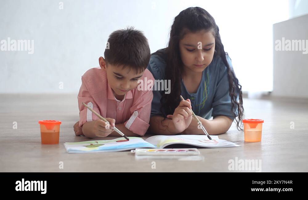 Little boy and little girl paint with paint on album lying on the floor