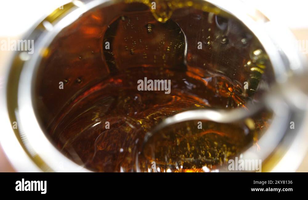 golden syrup pouring into a metal container, with a stirring spoon, a