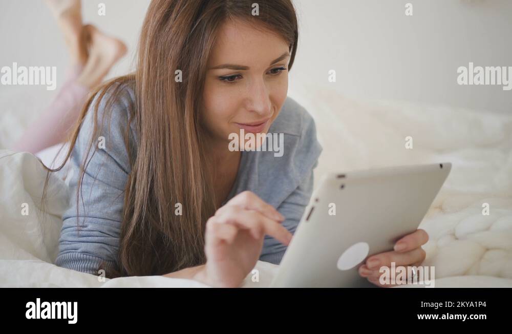 Woman in blue shirt with brown hair lying on the bed with white sheets