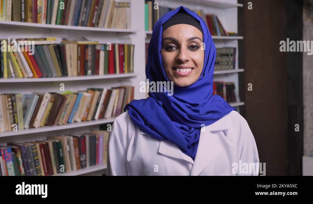 Young happy muslim woman in hijab standing in library and looking at ...