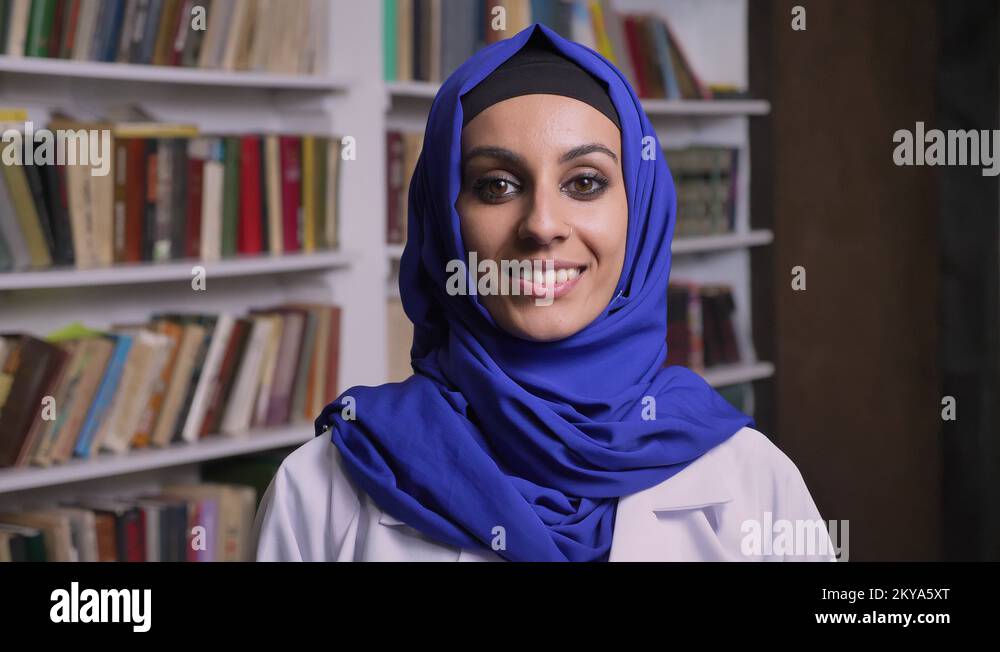 Young beautiful muslim woman in hijab standing in library and smiling ...
