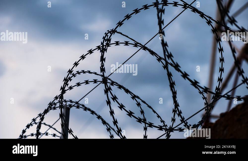 Barbed wire at the top of fence against the black, gloomy, dark sky ...