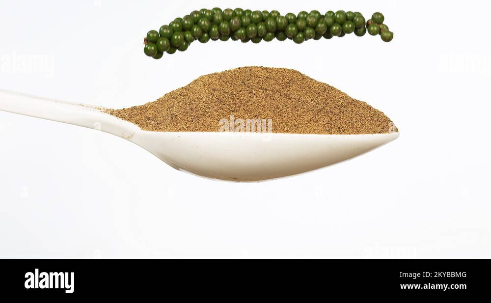 Fresh green pepper, piper nigrum, spice falling in pepper ground on