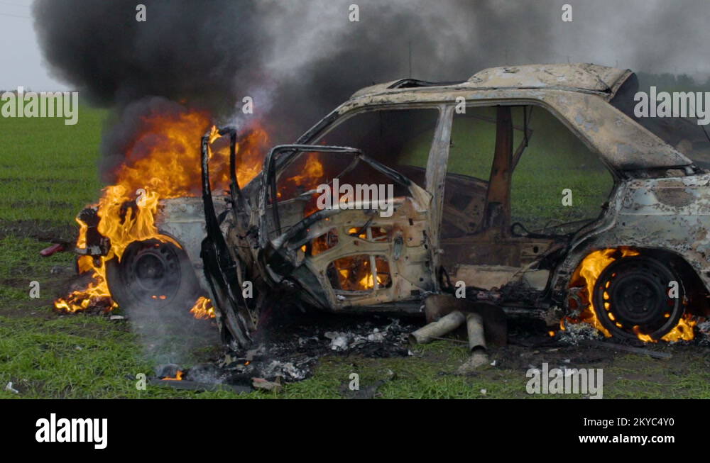 The burning car is in the field, the blown up car is on fire, the car