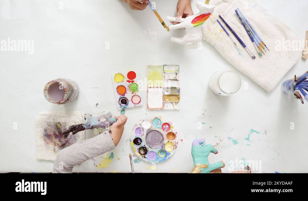 Little girls painting paper mache unicorn with acrylic paint Stock