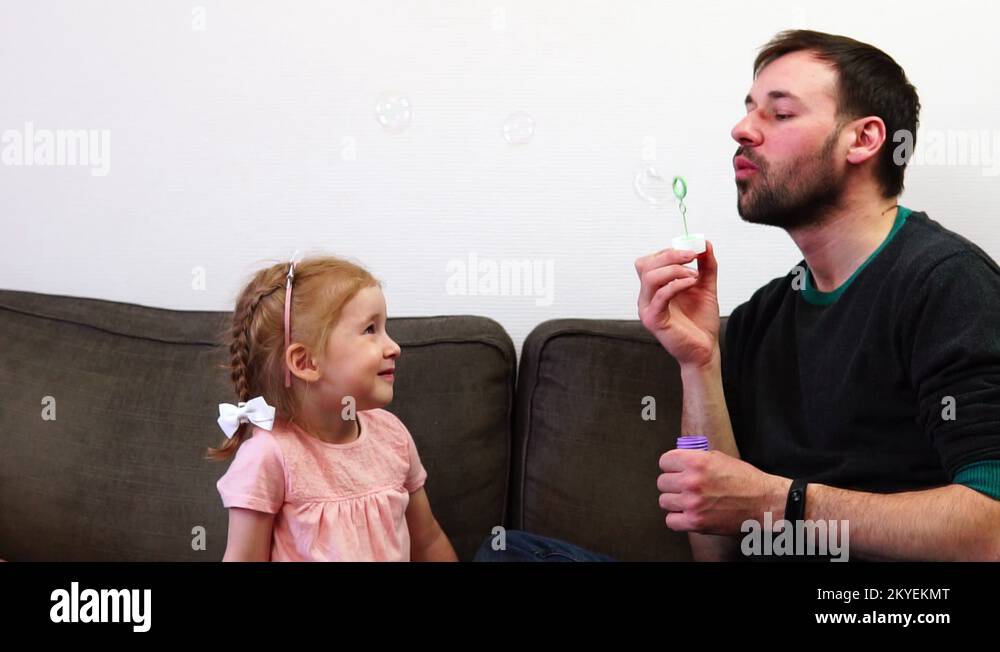 A pretty baby girl catches soap bubbles by her mouth. A father and his