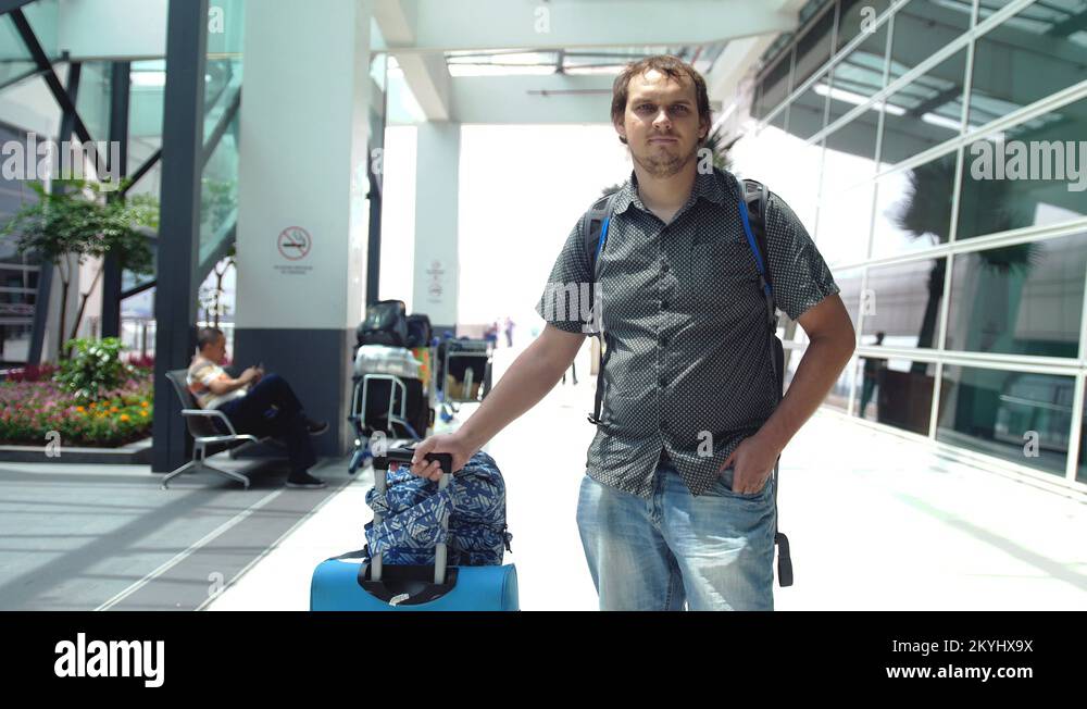 Young happy man with backpack pulling suitcase in modern airport