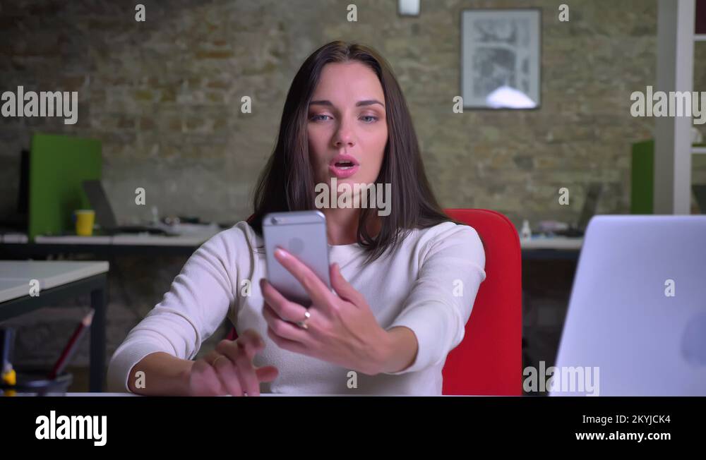 Woman talking via videochat using her smartphone, shows the office