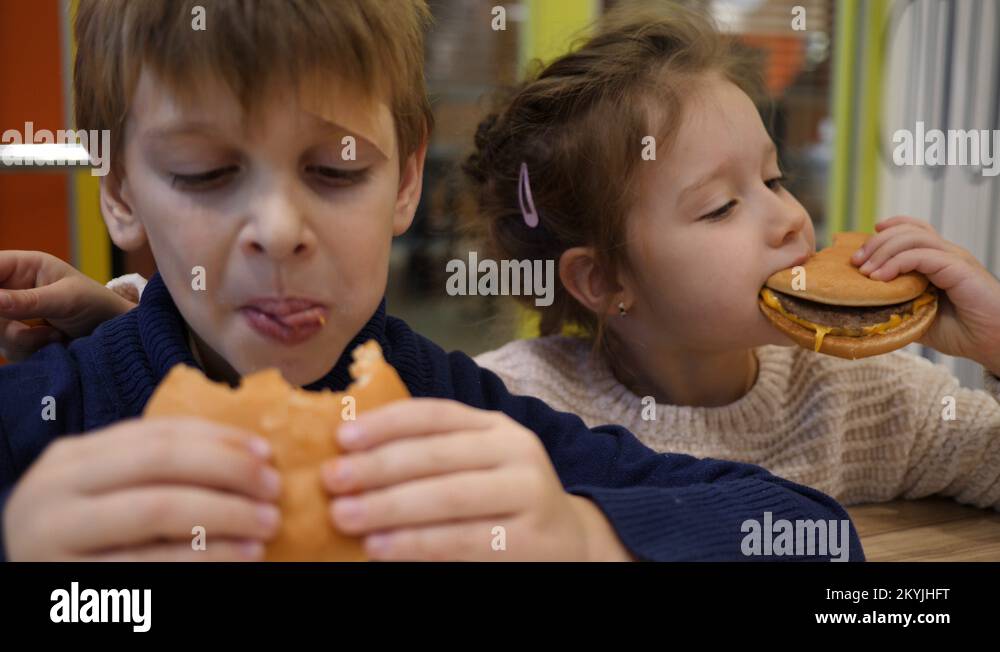 3 Hungry children greedily eating burgers boy and girl sit in fast food