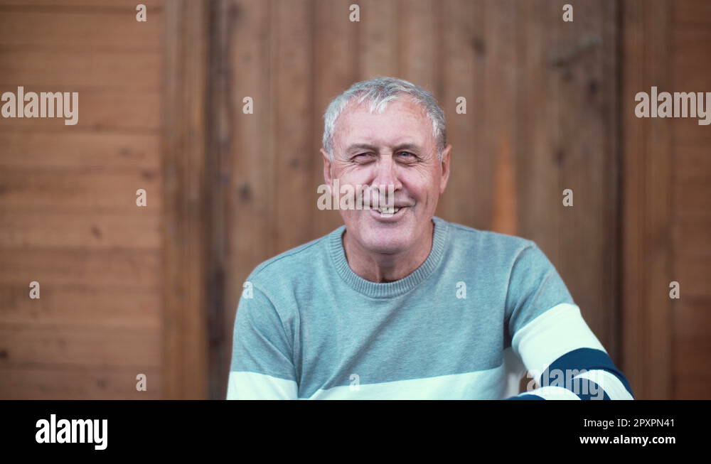 Old man sitting on the porch of the house. Grandfather making funny ...