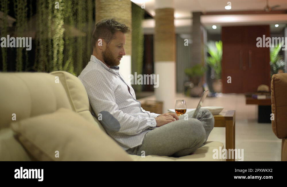 Man sitting on the sofa with his legs crossed and typing on laptop ...