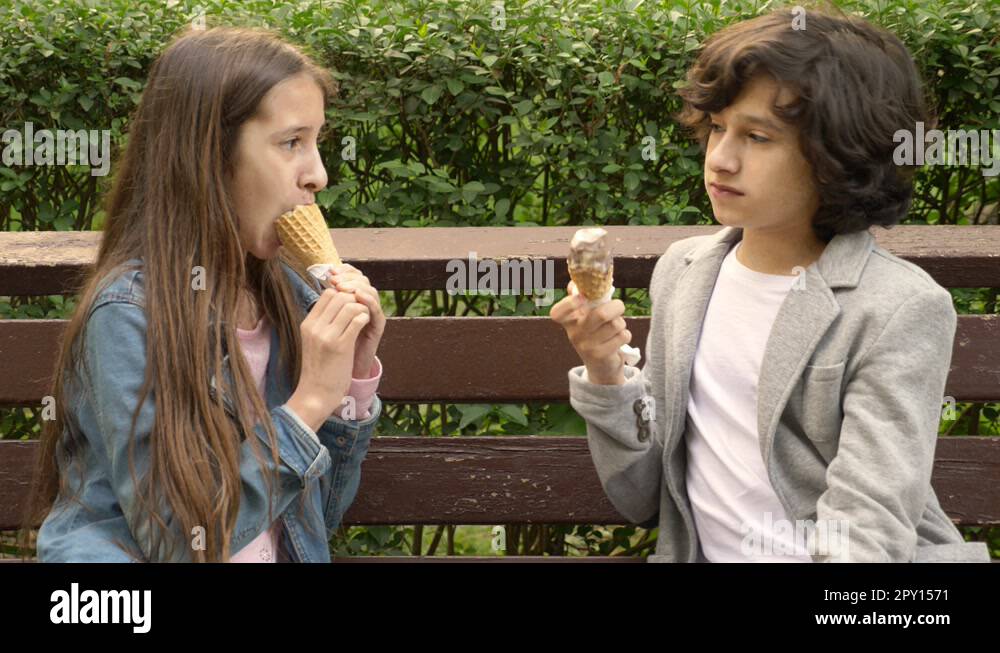 cute teenagers, boy and girl eating ice cream in the park and talking ...