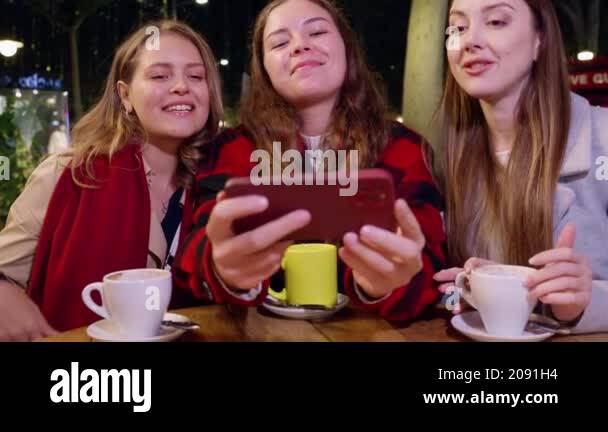 Three young women smiling and posing for a selfie while sitting at an ...