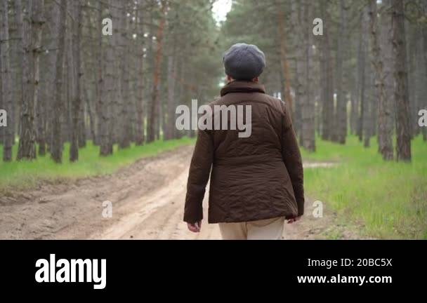 Back of person walking outside in green forest, senior woman walks ...