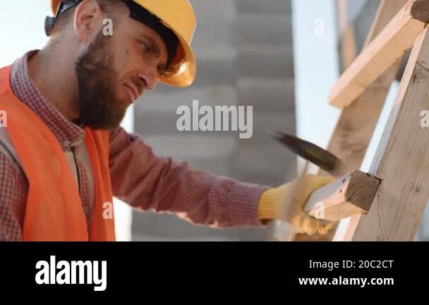 Construction worker uses hammer to secure wooden beams on site in clear ...