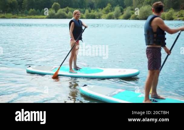 Slow motion young man and woman standing on sup board and swims surfing ...