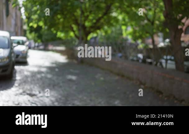 Defocused view of an outdoor cobblestone street in rome with trees and ...