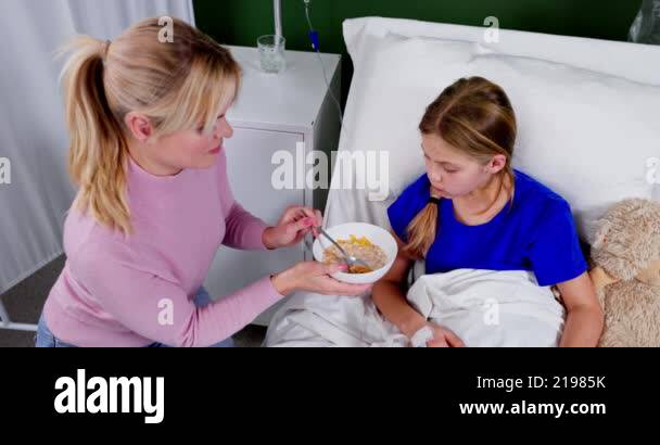 A caring mother feeds her sick daughter in a hospital bed, showing deep ...