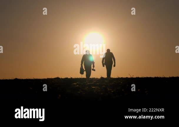 Silhouettes of two farmers walking across a field at sunrise or sunset ...