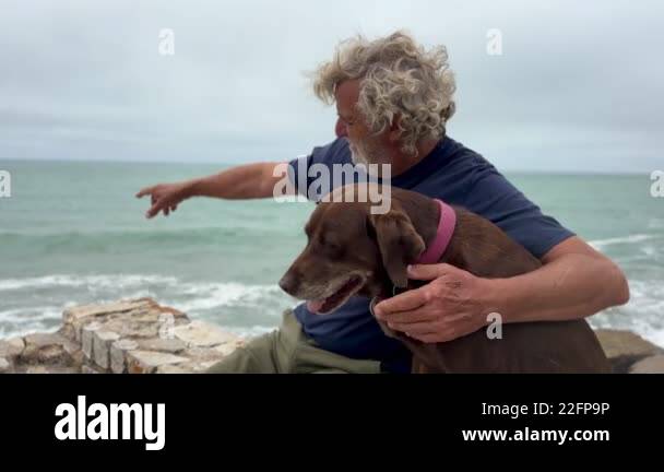 portrait of senior latino man bonding with his dog outdoors with ocean ...