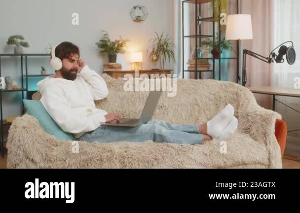 Happy relaxed Indian young man in wireless headphones sitting on sofa ...