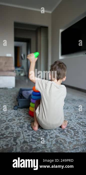 Rear view of a kid sitting near toy pyramid. Toddler puts the toy ...
