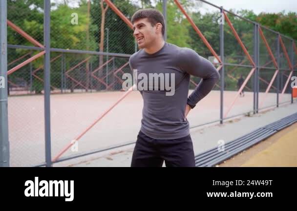 A man is standing in front of a fence with his hands on his hips ...